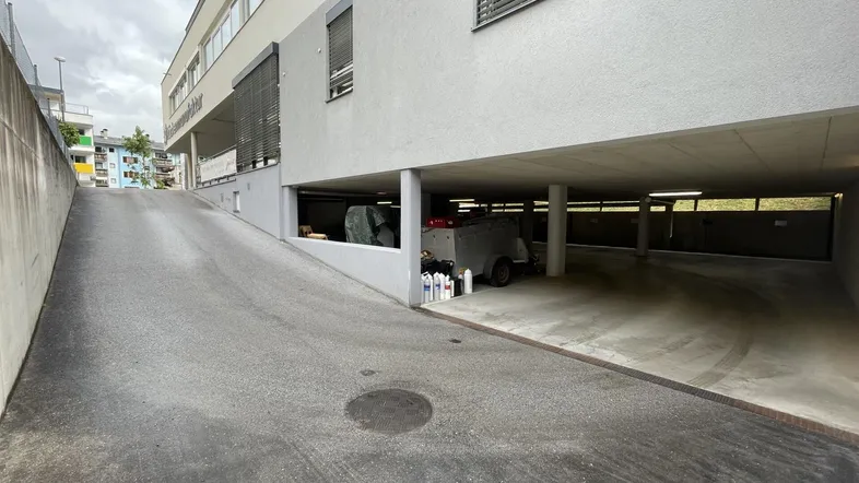 Zufahrtsrampe zu einer Tiefgarage unter einem modernen Gebäude mit Jalousien.
