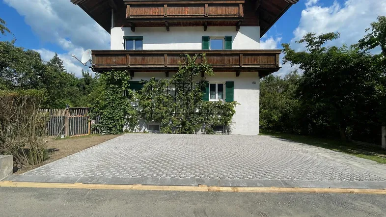 Traditionelles Haus mit Holzbalkonen und gepflasterter Einfahrt unter blauem Himmel.