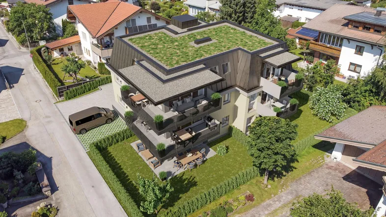 Luftaufnahme eines modernen Neubaus mit begrüntem Dach und Balkonen in einer Wohngegend mit Bergblick.