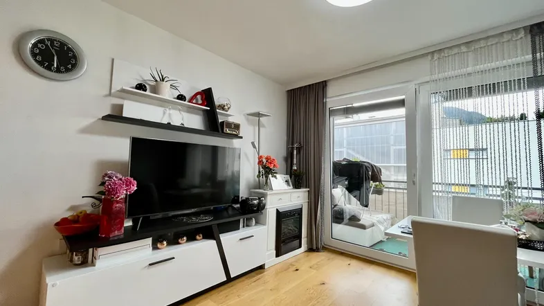 Helles Wohnzimmer mit modernem TV-Möbel, Holzboden und Zugang zu einem Balkon.