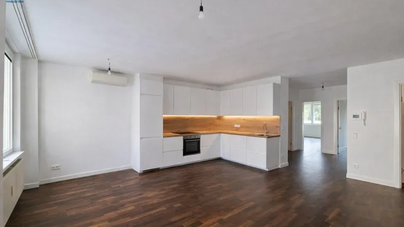 Geräumiger Wohnbereich mit moderner Einbauküche und dunklem Parkettboden, ideal für offenes Wohnen.