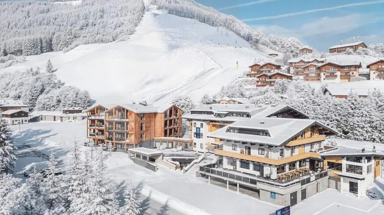 Winterliche Luftaufnahme eines modernen Gebäudekomplexes in einer verschneiten Berglandschaft.