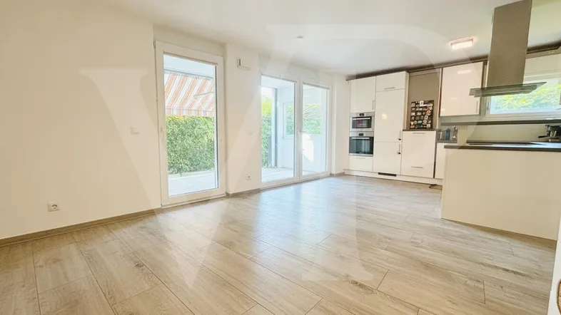 Heller offener Wohnbereich mit integrierter Küche, modernen Geräten und Zugang zur Terrasse.