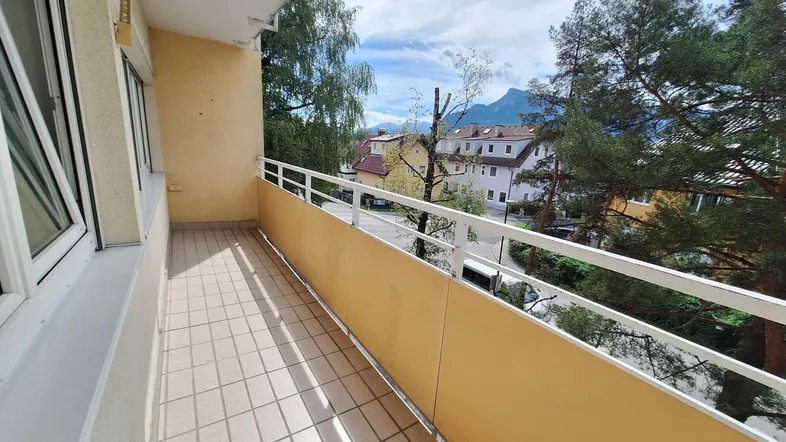 Heller Balkon mit Fliesenboden, gelbem Sichtschutz und weitem Blick auf die Berge und Umgebung.