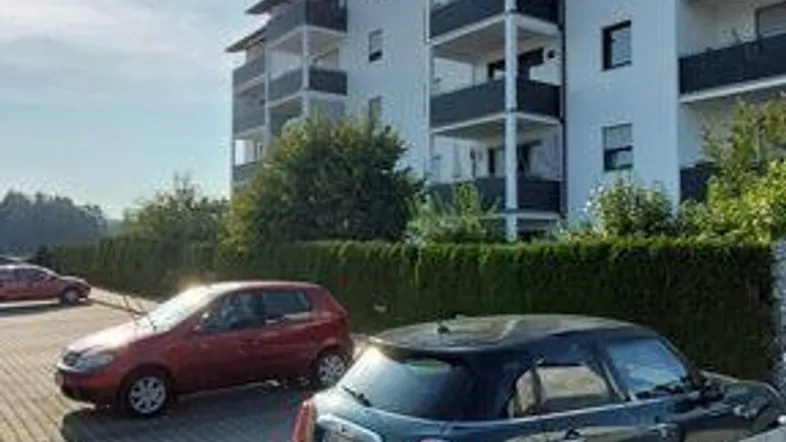 Mehrstöckiges Wohngebäude mit modernen Balkonen, weißer Fassade und Außenparkplätzen unter blauem Himmel.