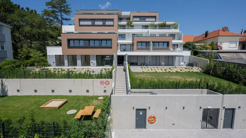 Modernes Mehrfamilienhaus mit gestuften Terrassen, Balkonen und einem kleinen Spielplatz im Gartenbereich.