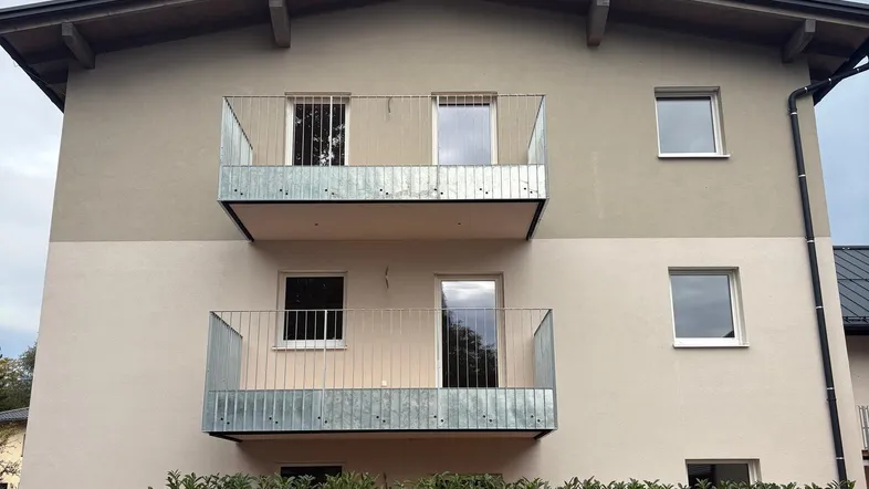 Modernes Mehrfamilienhaus mit zwei Balkonen und gepflegter Hecke im Vordergrund.