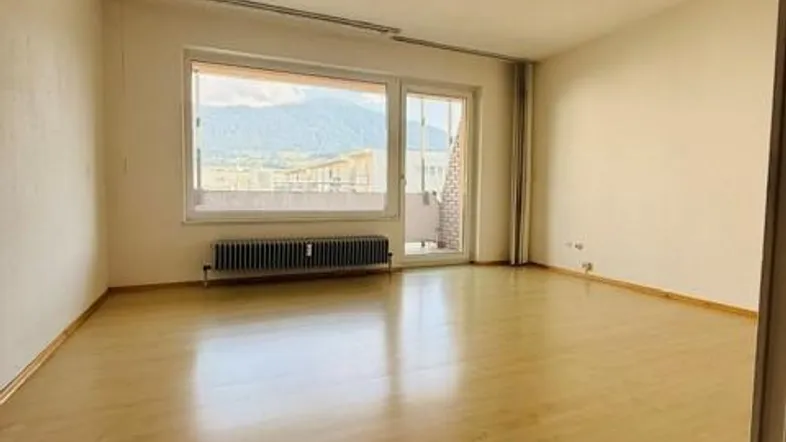 Helles Wohnzimmer mit Laminatboden, großem Fenster und Bergblick, bietet Zugang zu einem Balkon.