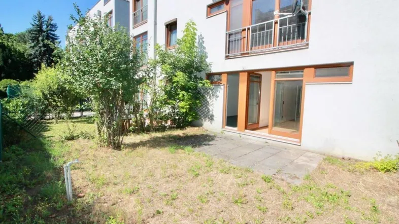 Außenbereich des Gebäudes mit einer kleinen gepflasterten Terrasse und einem Garten.