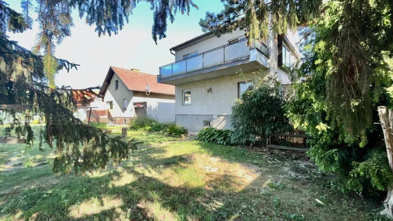 Seitenansicht des Hauses mit Gartenbereich und altem Baumbestand im Vordergrund.