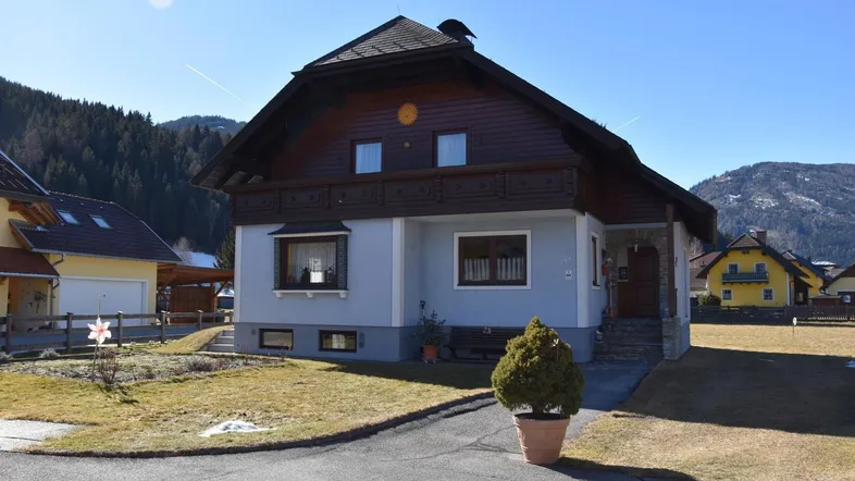 Traditionelles Haus mit Holzfassade und Vorgarten, umgeben von einer malerischen Berglandschaft.