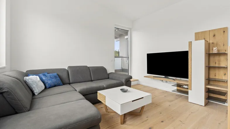 Gemütliches Wohnzimmer mit großem Sofa, Fernseher und Zugang zu einem Balkon.