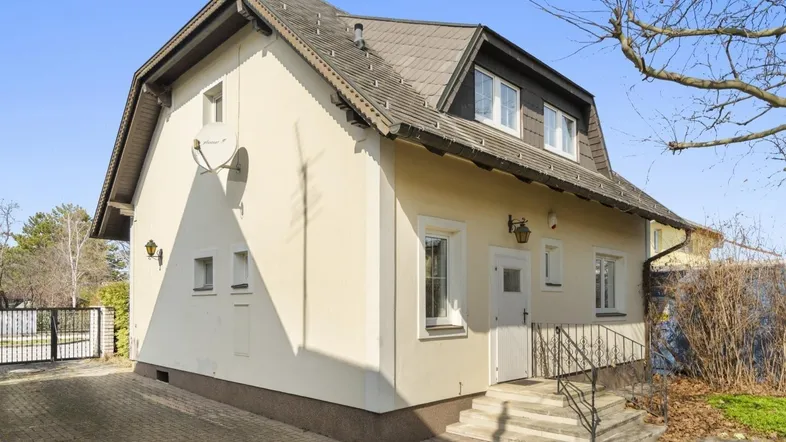 Traditionelles Einfamilienhaus mit gepflasterter Auffahrt und Mansarddach in ländlicher Umgebung.