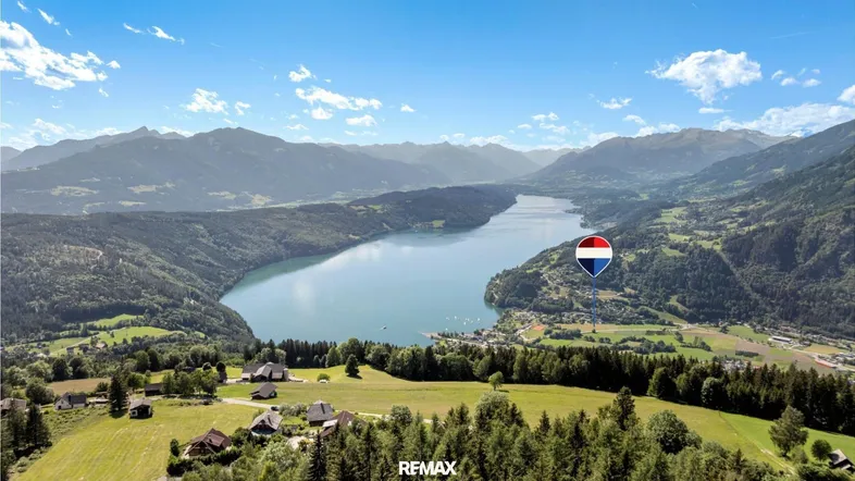 Atemberaubende Luftaufnahme eines Sees umgeben von grünen Bergen und kleinen Siedlungen.