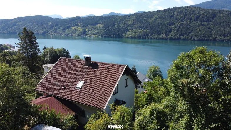 Luftaufnahme eines Hauses mit rotem Ziegeldach und weitem Blick auf den See und die Berge.