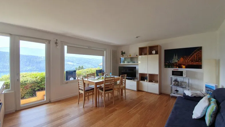 Heller Wohn- und Essbereich mit Holzboden und großen Fenstern mit Seeblick.