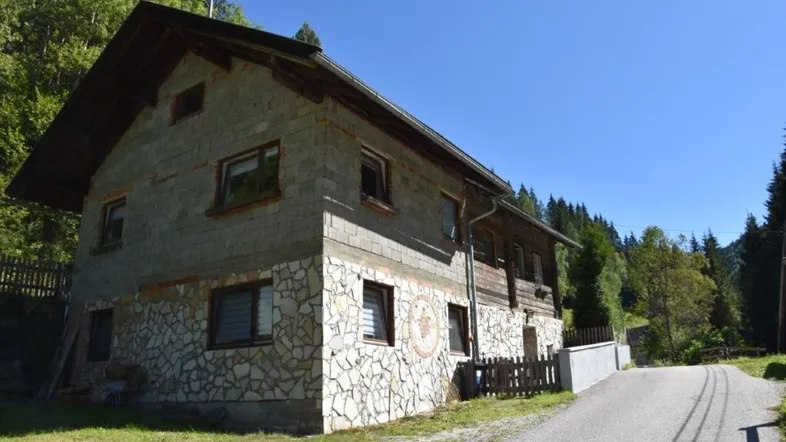 Ländliches Haus mit Steinfassade und Holzelementen in bergiger Umgebung.