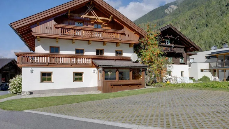 Traditionelles Alpenhaus mit Holzbalkonen und weißer Fassade vor bergiger Kulisse.