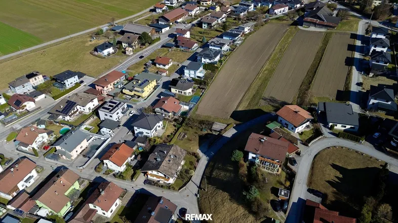 Panoramablick aus der Luft auf eine dichte Wohnbebauung neben landwirtschaftlich genutzten Feldern.