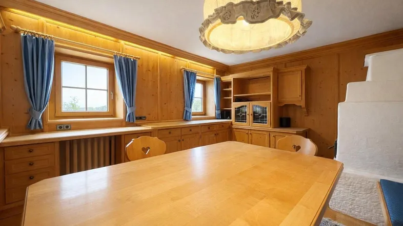 Traditioneller Essbereich mit Holztäfelung, großem Holztisch und einem Kachelofen, der eine gemütliche Atmosphäre schafft.