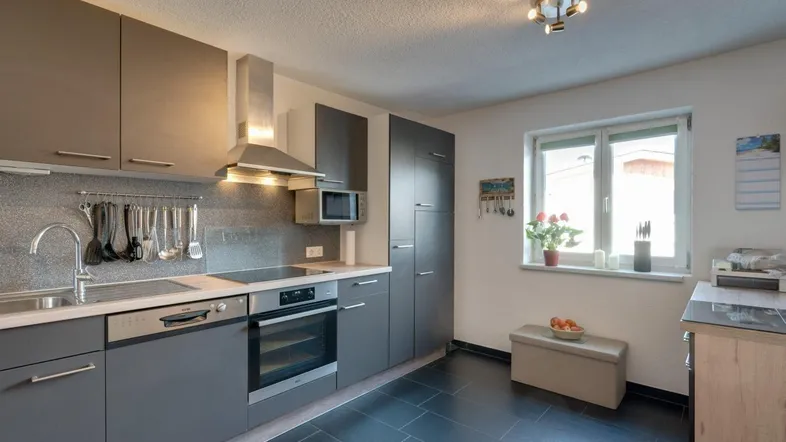 Moderne Küche mit grauen Schränken, schwarzen Fliesen und integrierten Geräten für den täglichen Gebrauch.