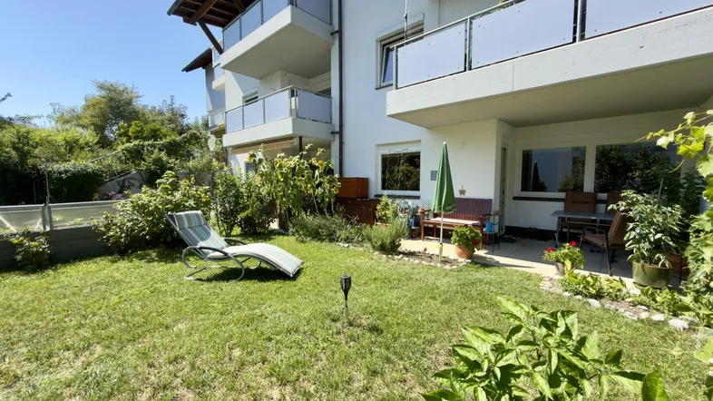 Gepflegter Gartenbereich mit Liegestuhl und Zugang zur Terrasse im Erdgeschoss eines Mehrfamilienhauses.