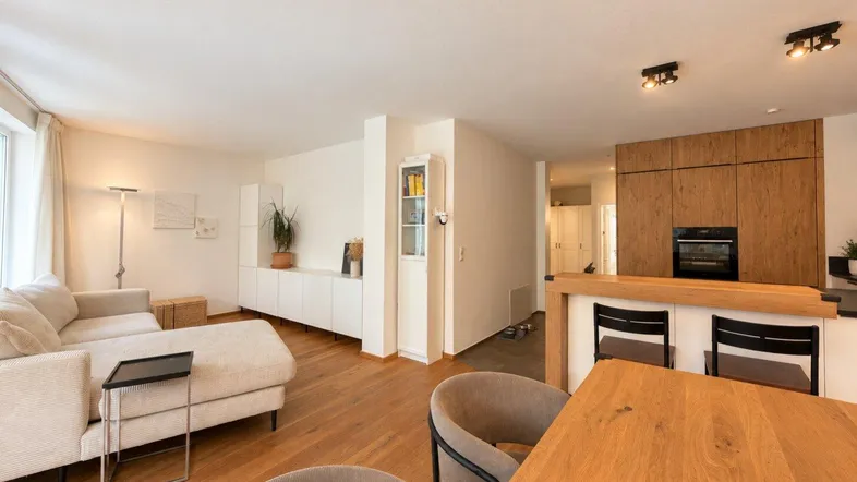 Heller offener Wohnbereich mit Holzboden, beigem Sofa und integrierter Küche.