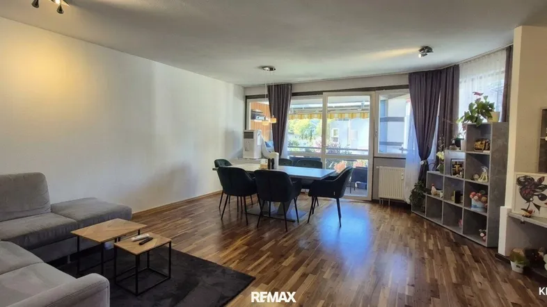 Geräumiger Wohn-Essbereich mit Holzboden, gemütlichem Sofa und Zugang zum Balkon.