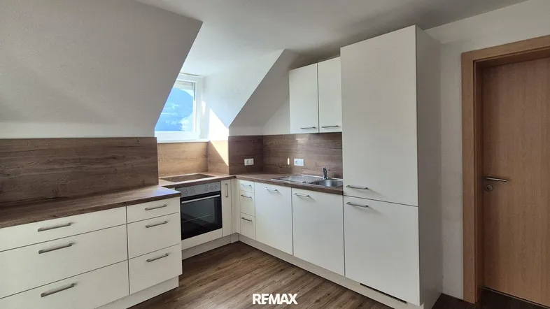 Moderne Einbauküche mit weißen Schränken, Holzoptik-Arbeitsplatten und Dachschrägenfenster.