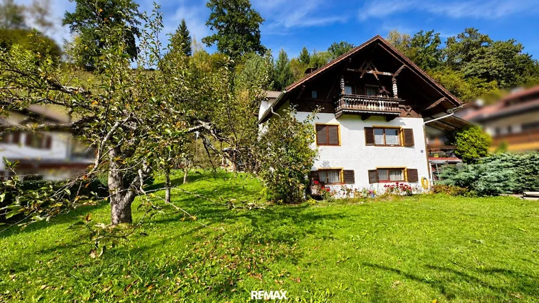 Charmantes Haus im alpinen Stil mit großem Garten und Obstbäumen in grüner Umgebung.