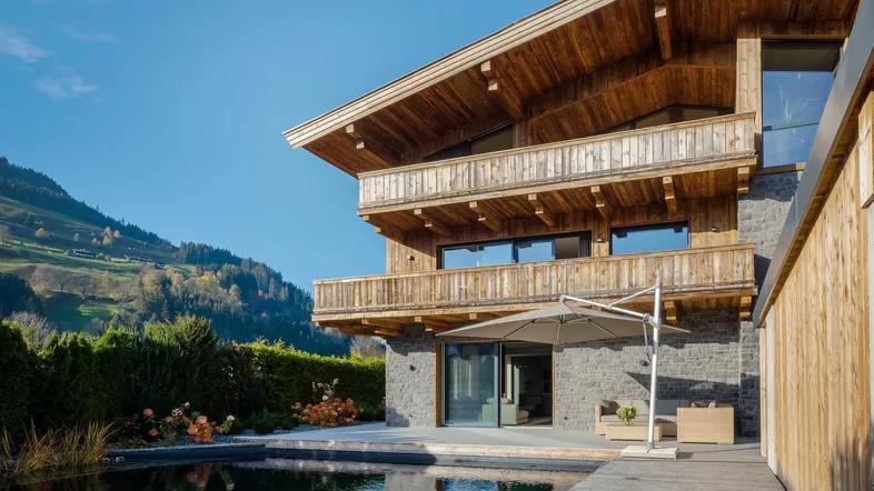 Modernes Chalet mit Holzfassade, Naturstein und Außenpool in alpiner Landschaft.
