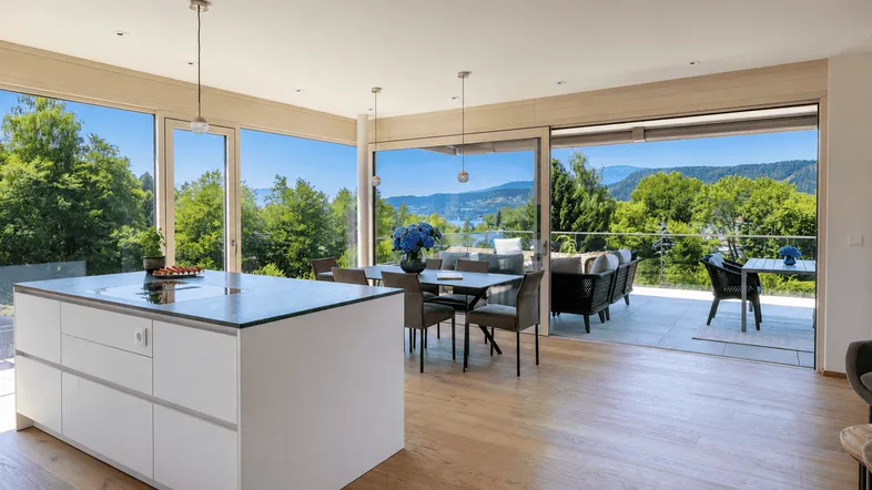 Heller, offener Wohn- und Essbereich mit moderner Küche, Holzboden und Zugang zur Terrasse mit Seeblick.