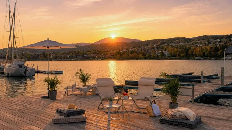 Holzsteg mit gemütlichen Sitzgelegenheiten und Blick auf den See bei Sonnenuntergang, umgeben von Bergen.