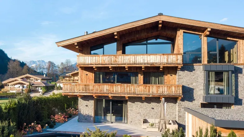 Modernes Chalet mit Holzfassade, Steinmauern, Balkonen und einem Naturpool im Gartenbereich.
