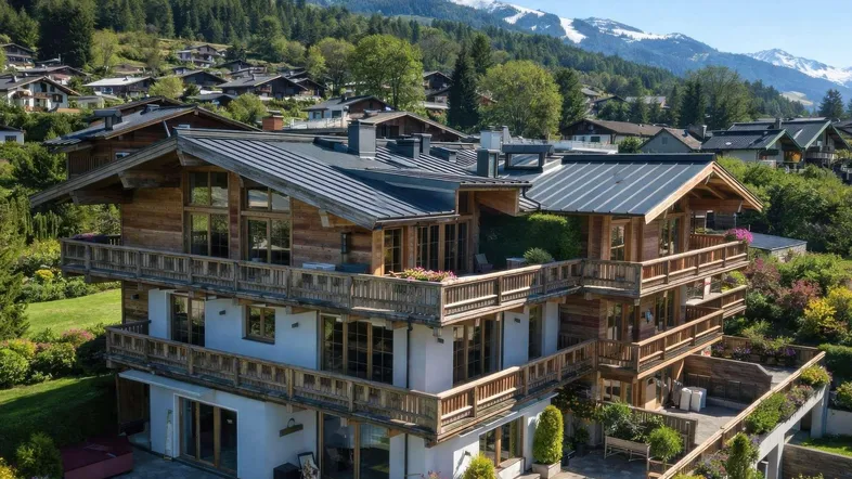 Großes Chalet im alpinen Stil mit mehreren Balkonen, Terrasse und Bergblick, umgeben von grünen Gärten.