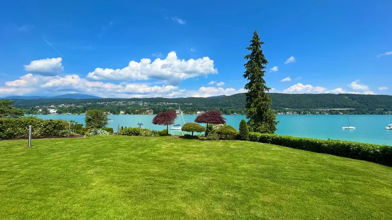 Gepflegter Rasenbereich mit malerischem Blick auf den See und die umliegende Berglandschaft unter blauem Himmel.