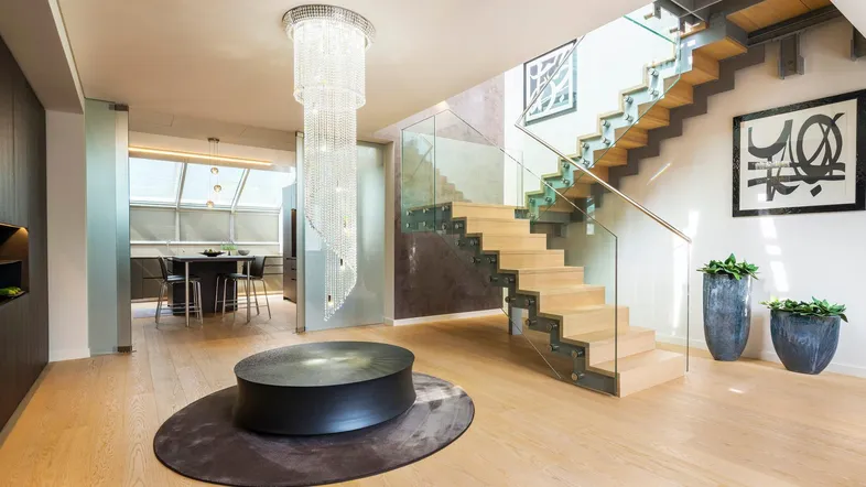 Großzügiger, lichtdurchfluteter Wohnbereich mit eleganter Holztreppe, Glasgeländer und modernem Kronleuchter.