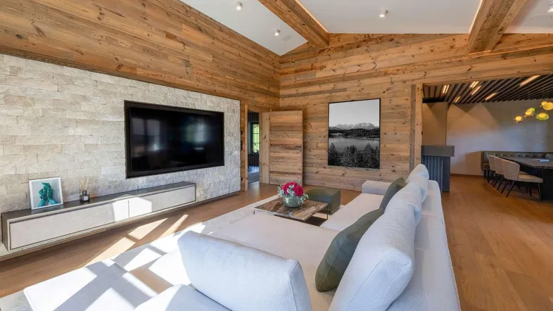Geräumiges Wohnzimmer im alpinen Stil mit Holzwänden, Steinakzenten und großem Flachbildfernseher.