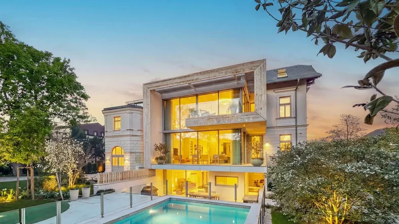 Moderne Villa mit großem Pool und gepflegtem Gartenbereich bei Sonnenuntergang, kombiniert traditionelle und moderne Architektur.