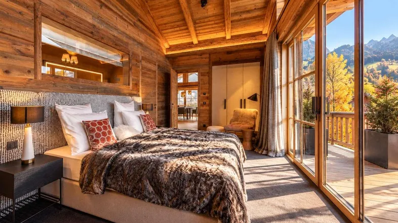 Gemütliches Schlafzimmer mit Holzwänden, großen Fenstern und direktem Zugang zum Balkon mit Bergblick.