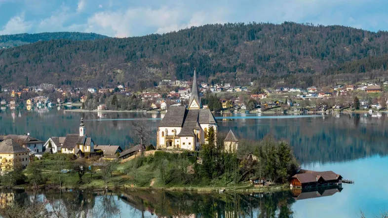 Malerische Ansicht eines Sees mit einer Kirche auf einer Insel und bewaldeten Bergen im Hintergrund.