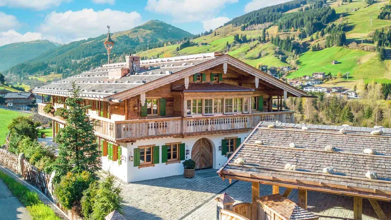 Traditionelles Alpenchalet mit Holzbalkonen und grünen Fensterläden, eingebettet in eine malerische Berglandschaft.
