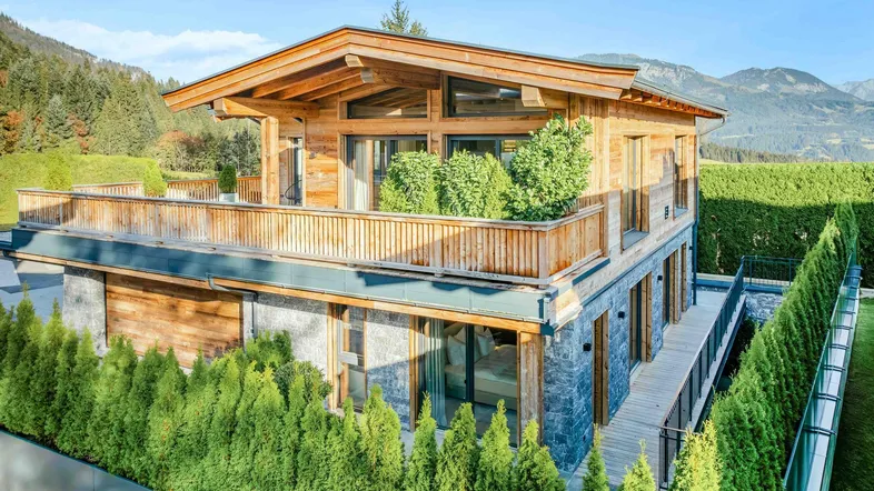Exklusives Chalet im alpinen Stil mit Holz- und Steinfassade, großem Balkon und Panoramablick auf die Berge.