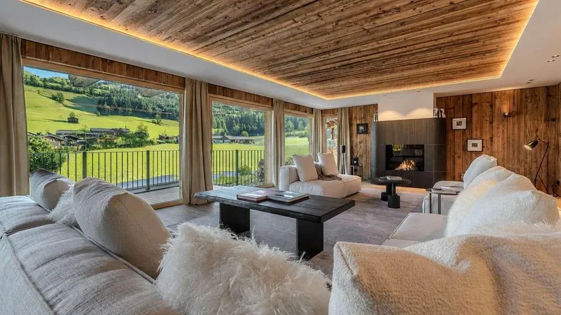 Helles Wohnzimmer im alpinen Stil mit Holzbalkendecke, Kamin und weitem Blick ins Grüne.