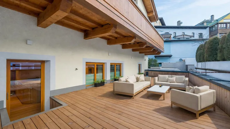 Große Holzterrasse mit bequemen Gartenmöbeln und Blick auf die umliegenden Gebäude.