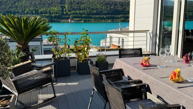Geräumige Terrasse mit Esstisch, Pflanzen und herrlichem Blick auf den See und die Berge.