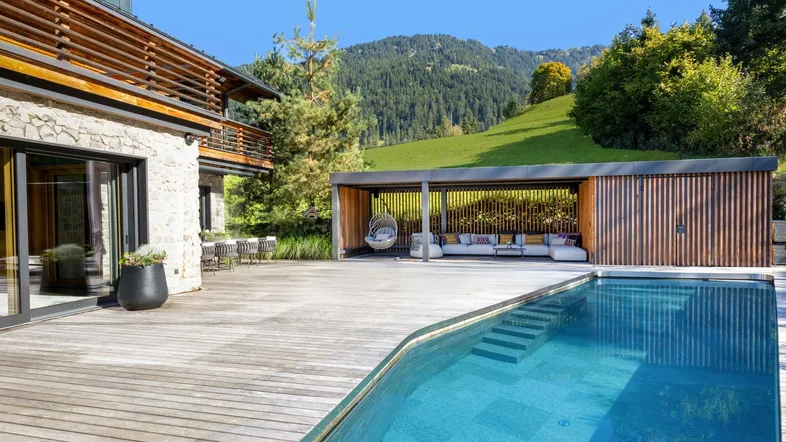 Großzügige Holzterrasse mit Pool, überdachtem Loungebereich und herrlichem Bergblick.