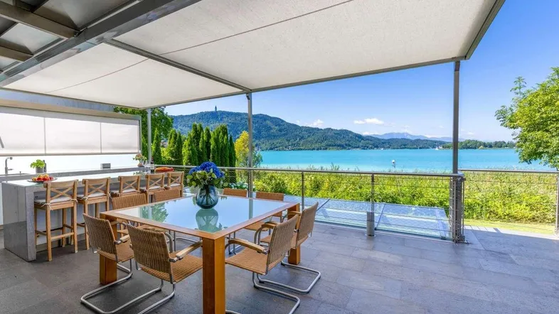 Große überdachte Terrasse mit Esstisch, Außenküche und atemberaubendem Blick auf den See und die Berge.