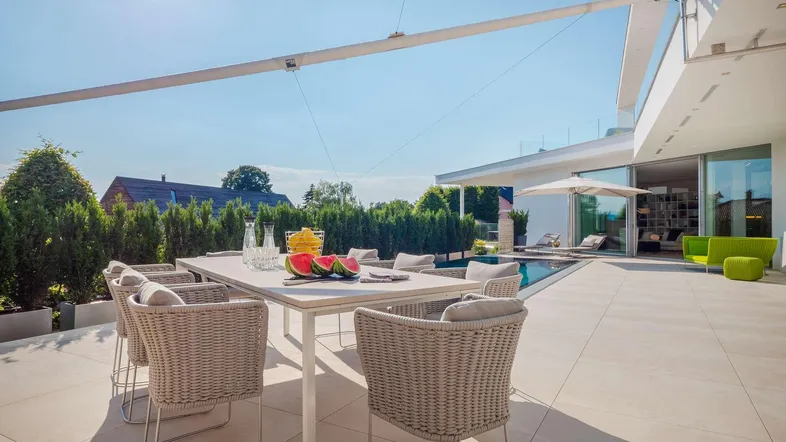 Moderne Terrasse mit Esstisch, Korbstühlen und Blick auf den Pool und die umliegende Landschaft.