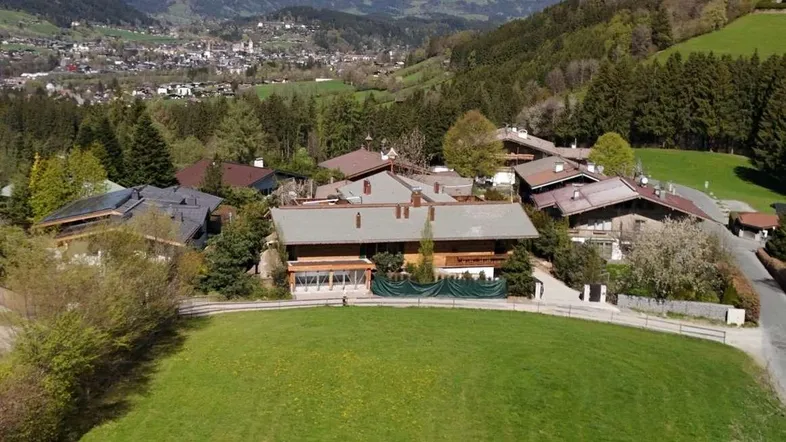 Luftaufnahme einer Wohnsiedlung mit traditionellen Häusern und beeindruckendem Alpenpanorama.
